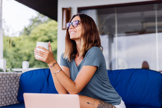 家快乐的白种女人在家里用笔记本电脑做远程工作舒服的地方喝茶电脑技术房子
