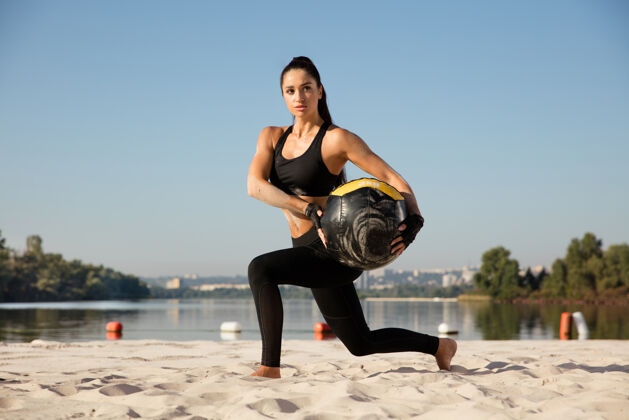 运动年轻健康的女子在沙滩上带球做弓箭步肌肉成年人健美运动员