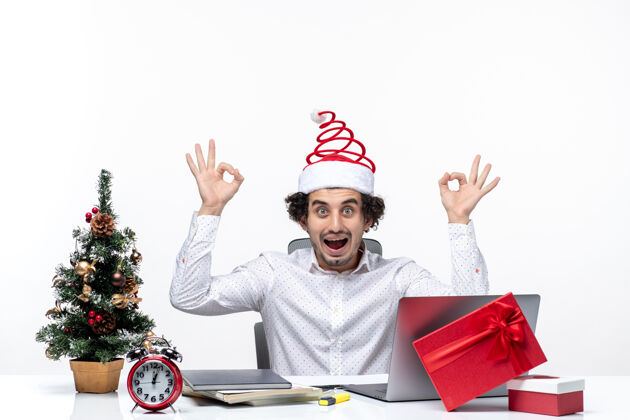 手势快乐积极向上的年轻商人 戴着滑稽的圣诞老人帽子 在白色背景的办公室里做着戴眼镜的手势年轻的商人眼镜人