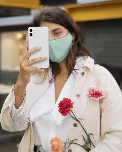 面罩拿着鲜花用智能手机拍照的女人正常大流行垂直