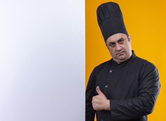 墙自信的中年男厨师 身着厨师制服 手举白墙 大拇指竖立在黄色墙上 留有复印空间厨师厨师抱着