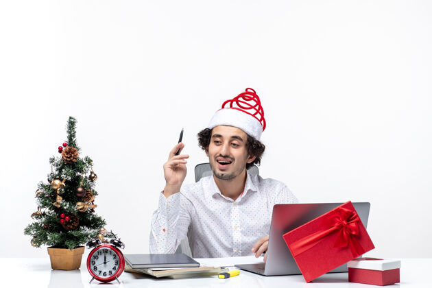 笔记好奇的年轻商人戴着有趣的圣诞老人帽 在白色背景的办公室里查看笔记和庆祝圣诞节庆祝办公室圣诞老人