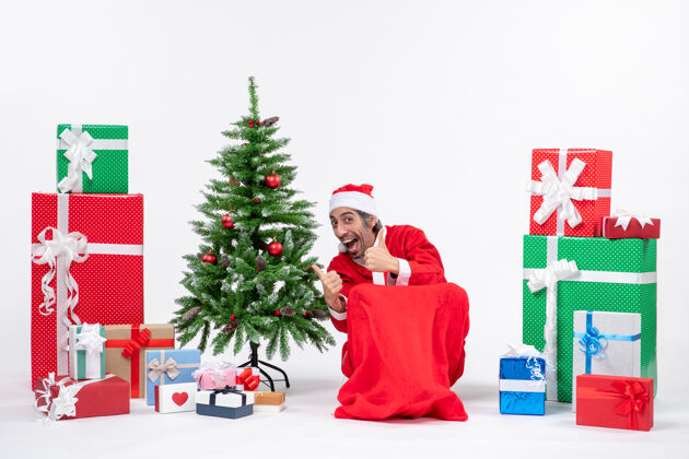 礼物情绪激动的年轻人装扮成圣诞老人 带着礼物和装饰圣诞树 在白色背景上做出ok手势情绪化年轻人男人