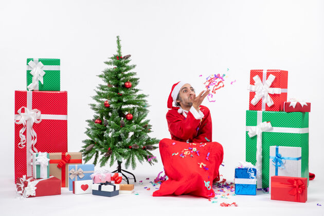 玩节日气氛与有趣的圣诞老人坐在地上玩圣诞装饰附近的礼物和装饰圣诞树白色背景礼物圣诞地面