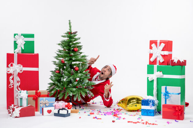 冬青圣诞气氛与震惊的圣诞老人躲在圣诞树附近的礼物在白色背景上不同的颜色圣诞老人不同礼物