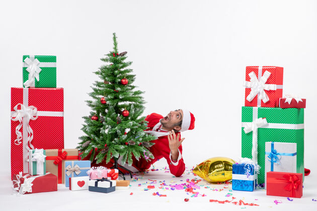 圣诞老人圣诞气氛与年轻的圣诞老人躲在圣诞树附近的礼物在白色背景上不同的颜色礼物年轻冬青