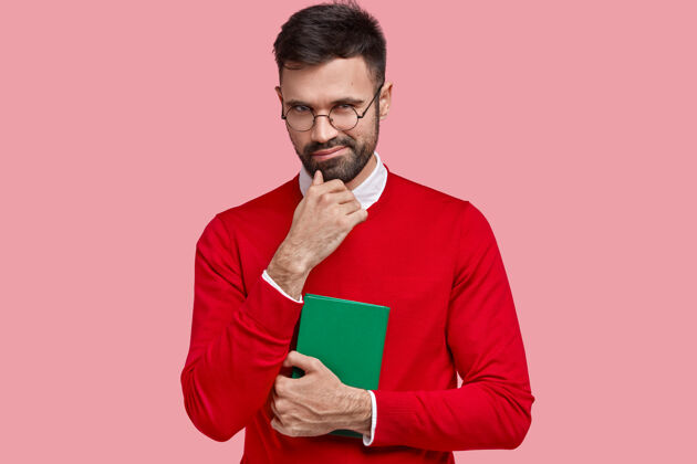 表情狡猾的男青年有心做事 托着下巴 背着绿色笔记本写笔记 穿着红色毛衣 戴着眼镜反应小学生眼镜
