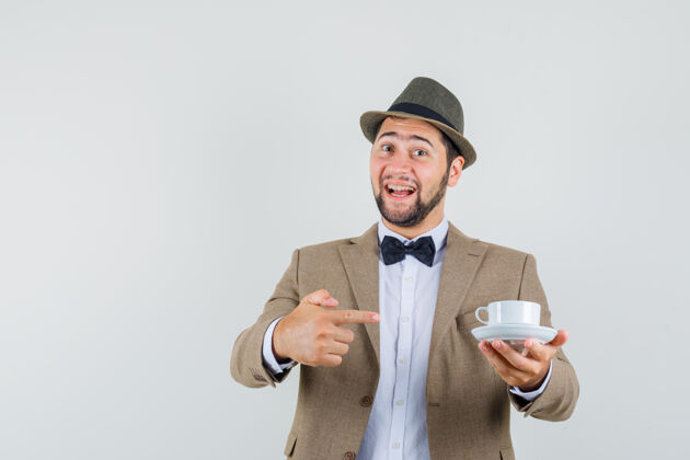 人穿西装的年轻人 戴着帽子 用茶托指着白色的杯子 看上去很高兴 眼前一亮人杯子茶碟