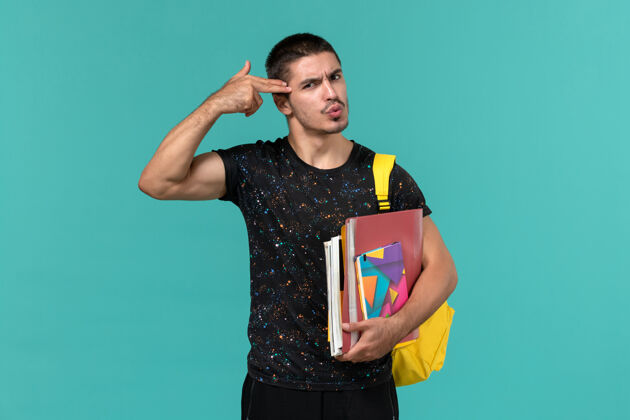 男性前视图中的男学生在黑暗的t恤黄色背包举行文案和文件在蓝色的墙上教训档案持有